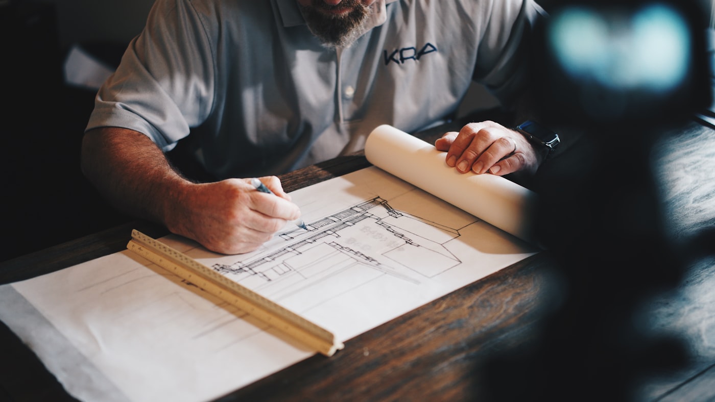 Designer hand-drafting a building elevation with a scale ruler